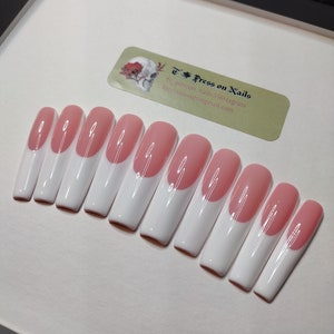 May include: A set of ten pink and white press-on nails with a half-moon design. The nails are arranged in a row on a white surface. The text "Press on Nails" is visible in the background.