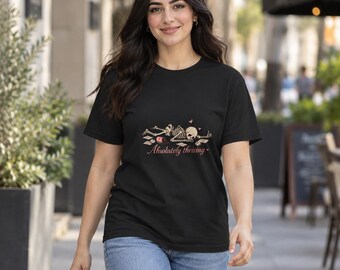 Puede incluir: Una camiseta negra de manga corta con un gráfico de un esqueleto tumbado rodeado de papeles esparcidos y una taza de café. El texto "Absolutely thriving" está impreso en una fuente cursiva debajo de la ilustración.