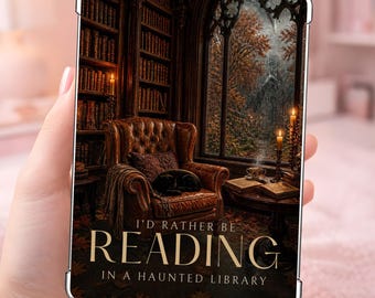 Puede incluir: Una funda rectangular para tableta con la imagen de un sillón de cuero en una biblioteca con estanterías, una ventana con árboles de otoño y velas. El texto dice I'D RATHER BE READING IN A HAUNTED LIBRARY en letras doradas.