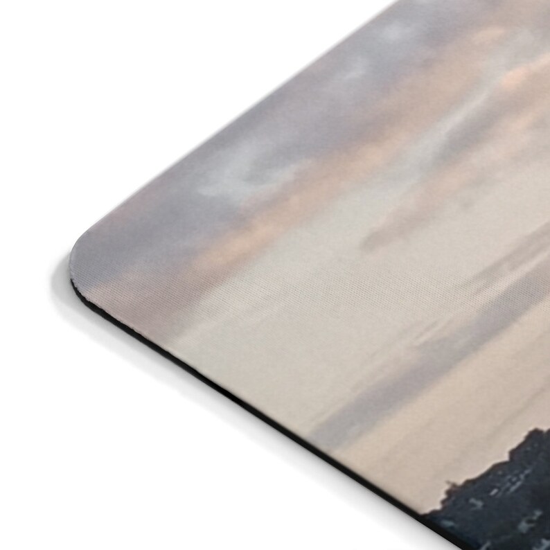 May include: A close-up of a gray and white mousepad with a soft, textured surface. The mousepad features a scenic image of a cloudy sky with a hint of pink and orange hues, suggesting a sunset or sunrise. The image is slightly blurred, creating a soft and dreamy effect.