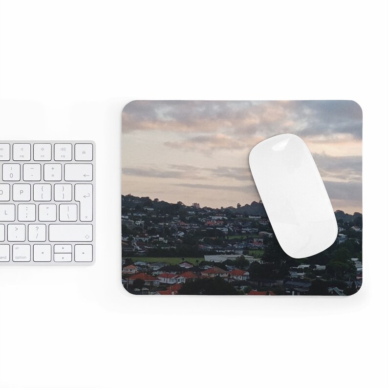 May include: A mousepad featuring a panoramic view of a city skyline at sunset. The city is nestled between hills and the sky is a soft pink and orange.
