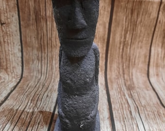 Könnte beinhalten: Eine schwarze Steinstatue einer Person mit einem großen Kopf und einem einfachen, abgerundeten Körper. Die Statue steht auf einem kleinen Sockel.