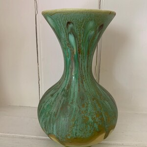 May include: A green and gold ceramic vase with a bulbous base and flared top. The vase has a glossy finish with a mottled pattern of green and gold. The rim is a lighter shade of green.
