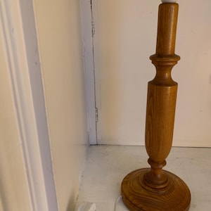 May include: A wooden table lamp with a light bulb socket. The lamp has a round base and a turned wooden stem. The lamp is made of light brown wood and has a white plug.