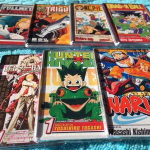 May include: A collection of eight colourful manga comic books, including Fullmetal Alchemist, Trigun, One Piece, Dragon Ball, Death Note, Hunter x Hunter, and Naruto. The books are all in Japanese and feature the first volume of each series.