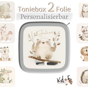 Könnte beinhalten: Ein quadratisches graues Toniebox-Gerät mit einem personalisierbaren Aufkleber, der den Namen Julius und ein Faultier-Motiv zeigt. Um das Gerät herum befinden sich acht einzelne quadratische Aufkleber mit verschiedenen Aquarell-Tieren, darunter ein Elefant, ein Einhorn, ein Tiger, ein Krokodil, ein Bär, ein Waschbär, ein Löwe und ein Igel.