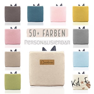 Könnte beinhalten: Eine Sammlung kleiner, quadratischer Stoffbeutel in verschiedenen Farben, darunter Grau, Türkis, Rosa, Gelb, Beige, Hellblau und Grün. Die Beutel haben eine schwarze Schleife oben und sind mit Namen wie "Carolina" und "Kid*E" personalisiert. Der Text "50+ FARBEN PERSONALISIERBAR" wird in der Mitte des Bildes angezeigt.