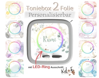 Puede incluir: Una pegatina cuadrada para reproductor de audio Toniebox con un recorte circular central para un anillo LED. El diseño muestra patrones florales de acuarela en tonos pastel suaves con detalles dorados y el nombre Rumi impreso en el centro.