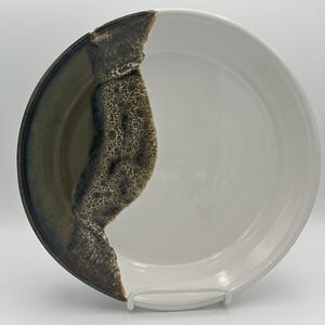 May include: A white ceramic serving dish with a dark green and brown glaze on one side. The glaze has a speckled pattern.