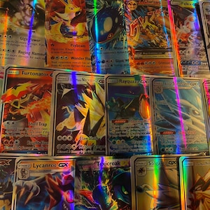 May include: A collection of holographic trading cards featuring various characters and designs. The cards display vibrant colors and text, with some cards showcasing the characters Charizard, Rayquaza, and Lucario. The cards are arranged closely together.