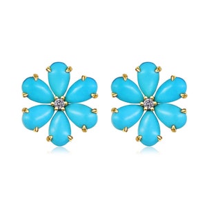 May include: A pair of flower-shaped stud earrings featuring six teardrop-shaped turquoise stones arranged around a central clear round gemstone. Each stone is set in a gold-toned metal prong setting, creating a symmetrical floral design.