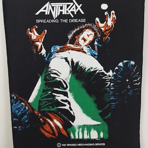 Peut inclure: Écusson noir avec le nom du groupe ANTHRAX en blanc et le texte « SPREADING THE DISEASE ». Le graphisme représente une personne tombant, avec des touches d'orange, de vert et de bleu. Copyright 1987 Bravado Merchandising Services.