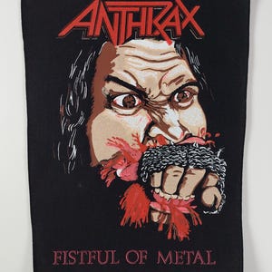 Könnte beinhalten: Schwarzer Aufnäher mit dem roten Bandnamen "ANTHRAX". Darunter eine Grafik einer geballten Faust in Ketten, mit Blut. Der Text "FISTFUL OF METAL" ist darunter gedruckt.