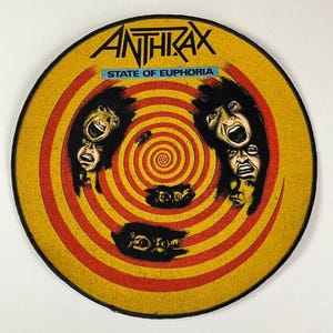 Könnte beinhalten: Runder Aufnäher mit dem Bandnamen "ANTHRAX" in Schwarz, über dem Text "STATE OF EUPHORIA" auf blauem Grund. Das Design zeigt eine gelb-rote Spirale mit schreienden Gesichtern.