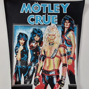 May include: Black patch featuring the band Mötley Crüe with the band's name in white and blue. The image shows four band members in colorful stage attire. The background is blue with a dotted border.
