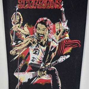 May include: Black patch featuring the band Scorpions with three band members playing instruments. The band's name is in red and gold letters at the top. The image has a red and yellow background.