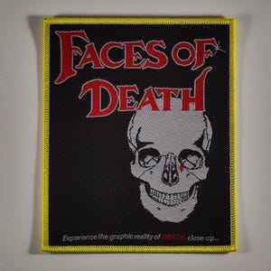 Könnte beinhalten: Schwarzer Aufnäher mit den roten Worten "FACES OF DEATH" über einer weißen Totenkopf-Grafik. Der Aufnäher hat einen gelben Rand und den Text "Experience the graphic reality of DEATH, close-up..." unten.