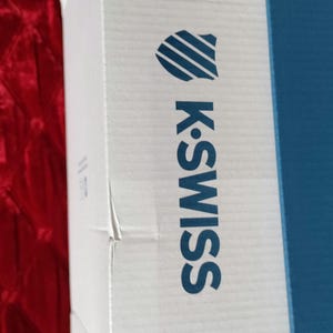 K&ouml;nnte beinhalten: Eine wei&szlig;e Box mit einem blau-wei&szlig;en Logo, auf dem "K-Swiss" steht. Die Box hat einen blauen Streifen auf der rechten Seite.