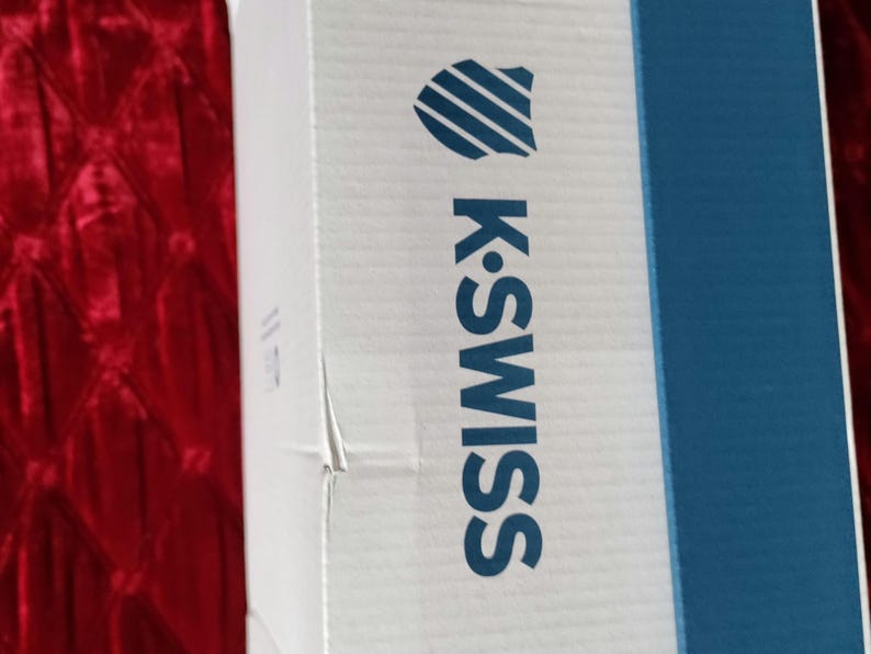 K&ouml;nnte beinhalten: Eine wei&szlig;e Box mit einem blau-wei&szlig;en Logo, auf dem "K-Swiss" steht. Die Box hat einen blauen Streifen auf der rechten Seite.
