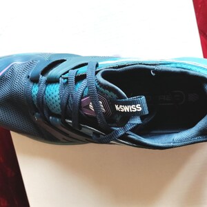 K&ouml;nnte beinhalten: Ein Paar blaue und t&uuml;rkisfarbene Sportschuhe mit einem wei&szlig;en K-Swiss-Logo an der Seite. Die Schuhe haben ein Mesh-Obermaterial und eine schwarze Sohle.