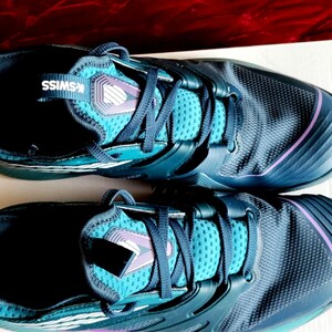 K&ouml;nnte beinhalten: Ein Paar dunkelblaue Sportschuhe mit t&uuml;rkisfarbenen Akzenten und einem wei&szlig;en K-Swiss-Logo. Die Schuhe haben ein strukturiertes Obermaterial und einen violetten Besatz.