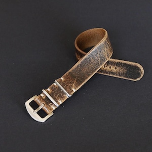 Könnte beinhalten: Ein braunes Lederarmband mit weißen Nähten und einer silbernen Schließe. Das Armband hat einen Used-Look, der ihm ein Vintage-Feeling verleiht.