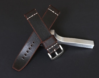 May include: A dark brown leather watch strap with white stitching. The strap has a silver buckle and is shown on a black surface.