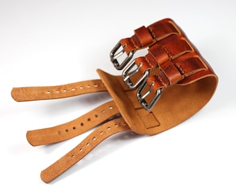 Peut inclure: Un bracelet de poignet en cuir marron avec trois sangles et des boucles argentées. Le bracelet comporte trois boucles et sangles supplémentaires pour le réglage. Le cuir a un aspect texturé.