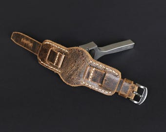 May include: A brown leather watch strap with white stitching and a silver buckle. The strap is distressed and has a vintage look.