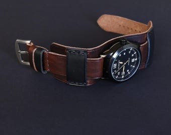 May include: A black-faced wristwatch with white numerals and hands, set in a brown leather cuff-style band. The band features a black leather accent and a silver buckle. The watch is displayed against a dark background.