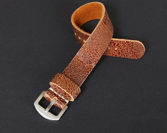 Puede incluir: Una correa de reloj de cuero marrón con una hebilla plateada. La correa tiene una superficie texturizada y granulada.