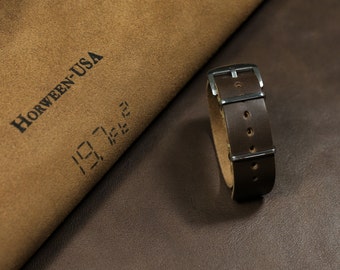 Puede incluir: Una correa de reloj de cuero marrón con herrajes plateados. La correa está hecha de cuero Horween, un cuero de alta calidad conocido por su durabilidad y longevidad. La correa se muestra sobre una superficie de cuero marrón.