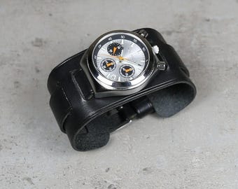 May include: A silver-faced wristwatch with black and orange accents is set on a wide, black leather cuff. The watch has a stainless steel case and a black leather band. The watch face displays multiple dials and hands.