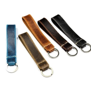 May include: Five leather keychains in different colors: brown, dark brown, black, blue, and light brown. Each keychain has a silver key ring.
