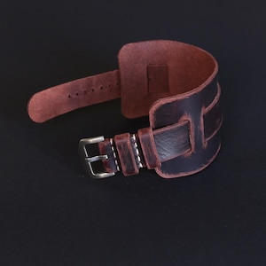 Peut inclure: Un bracelet de montre en cuir marron avec un aspect vieilli et une boucle argentée.