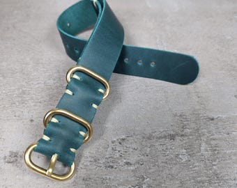 Könnte beinhalten: Ein teal-farbenes Leder-Uhrenarmband mit messingfarbener Hardware. Das Armband hat eine Schnalle und zwei Schlaufen mit weißen Nähten. Das Leder hat eine glatte Textur und ist für eine Uhr konzipiert.