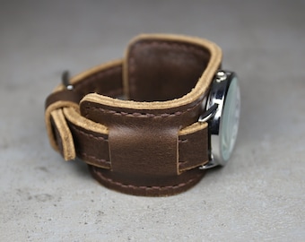 May include: A brown leather watch band with a tan stitching detail. The band is wrapped around a silver watch face.