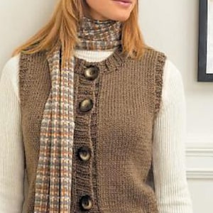 Puede incluir: Un chaleco de punto marrón con botones grandes y redondos. El chaleco se lleva sobre una camisa blanca de manga larga y se combina con una bufanda estampada. Un sombrero blanco completa el conjunto, creando un look acogedor y en capas.