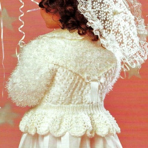 May include: A white crocheted cardigan with a ruffled hem and a bow at the back. The cardigan is worn over a white dress with a striped pattern.