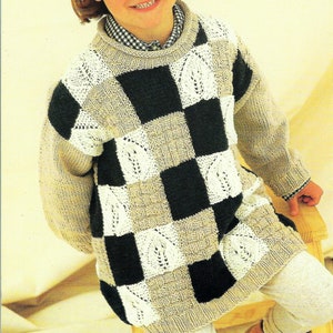 May include: A child wearing a beige and black checkered sweater with a white lace pattern. The sweater has a crew neck and long sleeves.