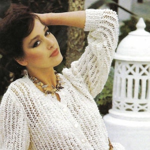 May include: A white crocheted cardigan with a button closure and long sleeves. The cardigan is worn with a brown leather belt.