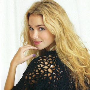 May include: A black crochet top with a delicate openwork pattern. The top has short sleeves and a cropped length. The model is wearing the top with a red skirt.