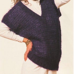 May include: A woman wearing a white long-sleeved shirt with a purple knitted sleeveless sweater over it. She is wearing gold jewellery and has her hair pulled back.