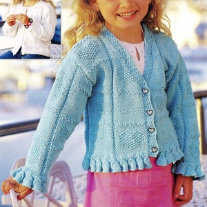 May include: A light blue knitted cardigan with a heart-shaped button fastening and a ruffled hem. The cardigan is being worn by a young girl with blonde hair.