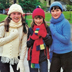 May include: Three girls wearing knitted hats, scarves, and gloves. The girl on the left is wearing a white hat, scarf, and gloves. The girl in the middle is wearing a red hat, scarf, and gloves. The girl on the right is wearing a blue hat, scarf, and gloves.