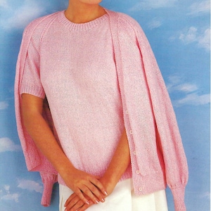 May include: A pink knitted sweater and cardigan set with short sleeves. The cardigan has a button closure.