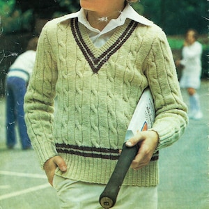 May include: A light green cable knit sweater with a burgundy and white v-neck collar. The sweater has a burgundy stripe across the bottom. A person is holding a wooden cricket bat.