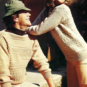May include: A couple wearing beige knitted sweaters with a cable knit pattern. The woman is wearing a green hat and the man is wearing a green bucket hat.