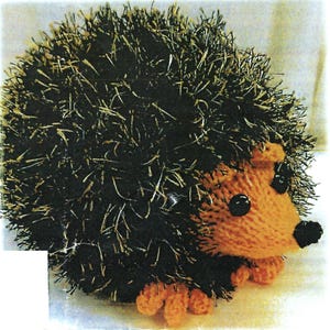 May include: A knitted hedgehog toy made with brown and orange yarn. The hedgehog has black eyes and a small black nose.
