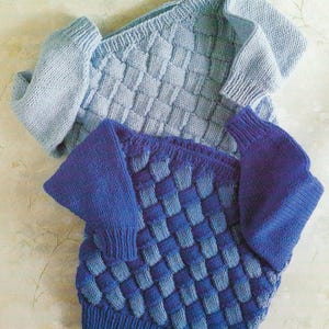 May include: Two knitted sweaters, one light blue and one dark blue, with a woven pattern. The sweaters have long sleeves and a crew neck.
